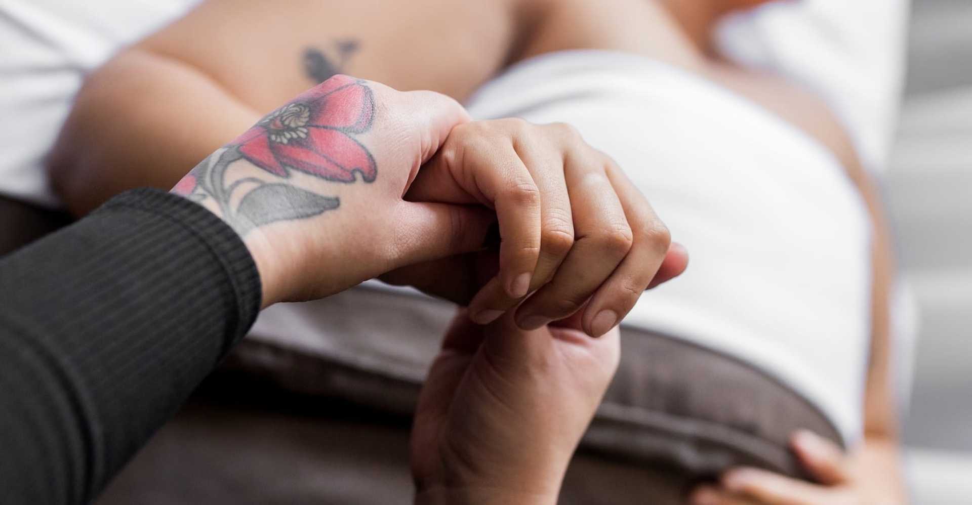 Two people holding hands, one has a vibrant flower tattoo on their wrist.