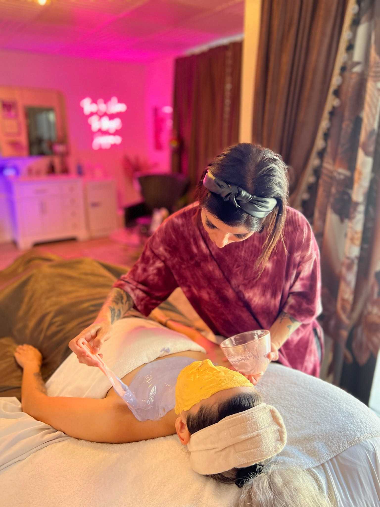 Spa treatment in progress; woman applying mask to client's face in calming environment.