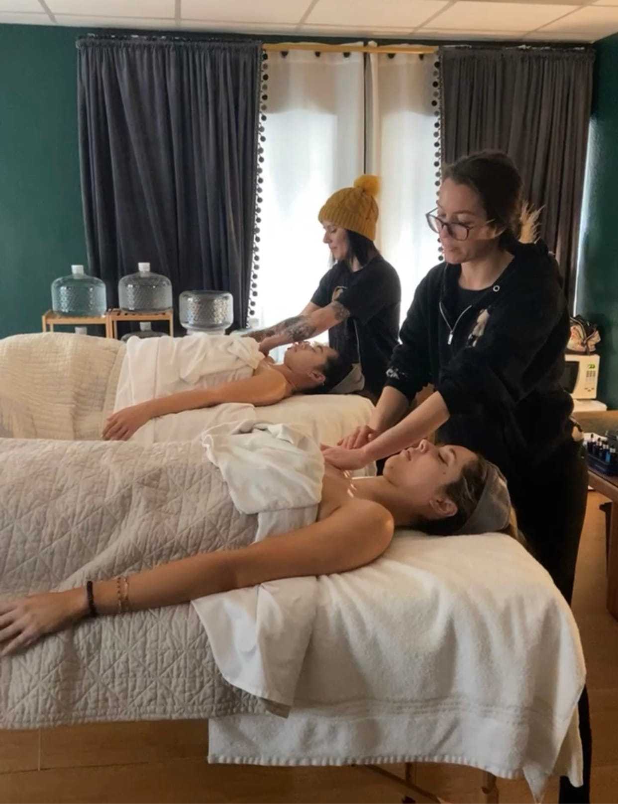 Two people receiving massages in a serene room with dark curtains.
